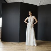 actress emmy rossum stands in a bare room in front of a black screen wearing a white grecian goddess gown