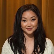 lana condor sits and smiles to the camera against a brown background