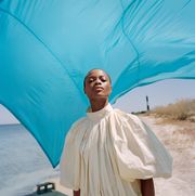model stands on beach in white dress in front of blue tarp